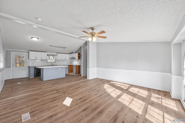 unfurnished living room with vaulted ceiling, ceiling fan, a textured ceiling, and light wood-type flooring