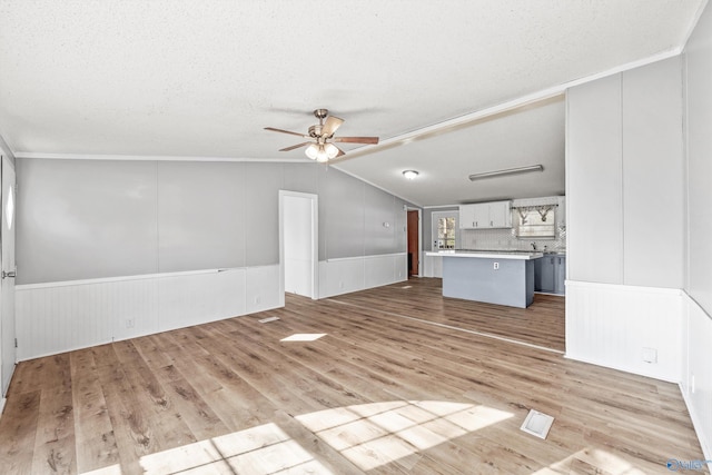 unfurnished living room with lofted ceiling, ceiling fan, light wood-type flooring, and a textured ceiling