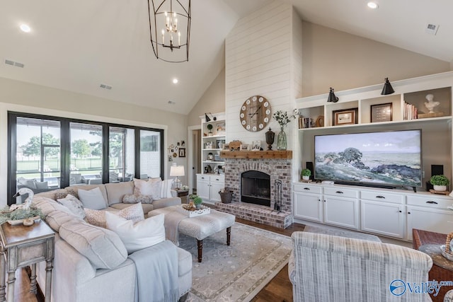 living room featuring hardwood / wood-style flooring, a chandelier, high vaulted ceiling, brick wall, and a brick fireplace