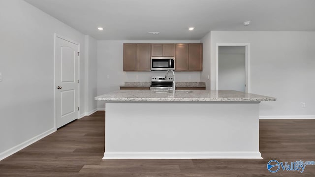 kitchen with appliances with stainless steel finishes, a kitchen island with sink, sink, and dark wood-type flooring