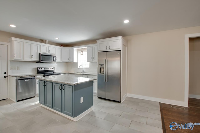 kitchen featuring sink, backsplash, stainless steel appliances, a center island, and white cabinets