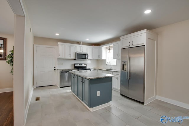 kitchen featuring a kitchen island, white cabinetry, sink, stainless steel appliances, and light stone countertops