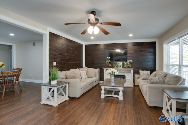 living room with dark wood-type flooring, wooden walls, and ceiling fan