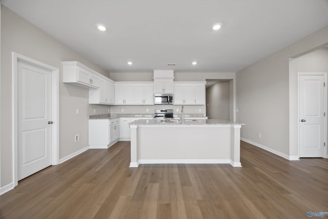 kitchen featuring appliances with stainless steel finishes, white cabinetry, a kitchen island with sink, light stone counters, and light wood-type flooring