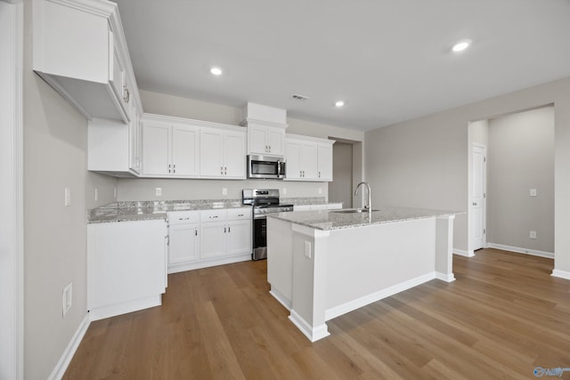 kitchen featuring sink, appliances with stainless steel finishes, light stone countertops, white cabinets, and a center island with sink