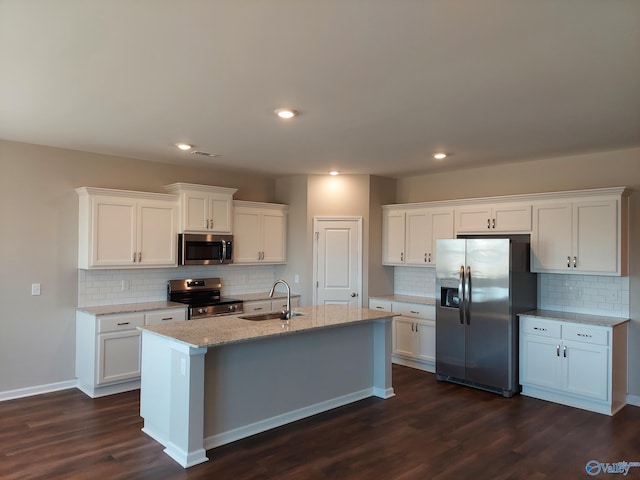 kitchen with sink, an island with sink, stainless steel appliances, light stone countertops, and white cabinets