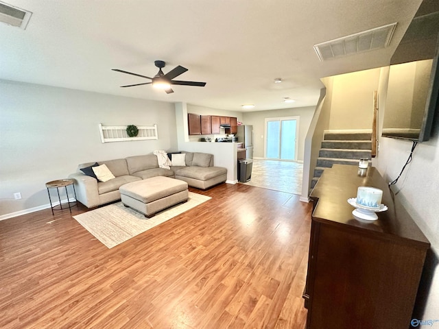 living room featuring light wood-style floors, visible vents, stairway, and baseboards