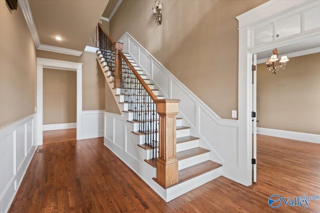 staircase with an inviting chandelier, crown molding, and hardwood / wood-style flooring