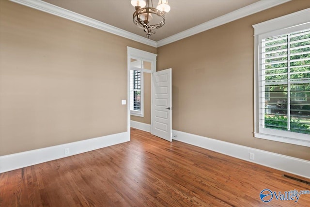 empty room with hardwood / wood-style flooring, ornamental molding, and a chandelier