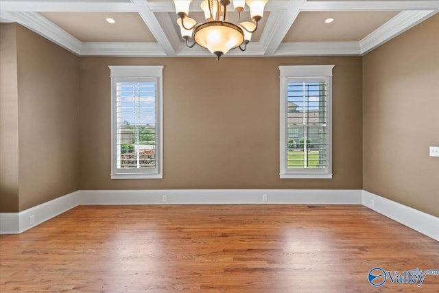 empty room with coffered ceiling, a notable chandelier, ornamental molding, and light hardwood / wood-style floors