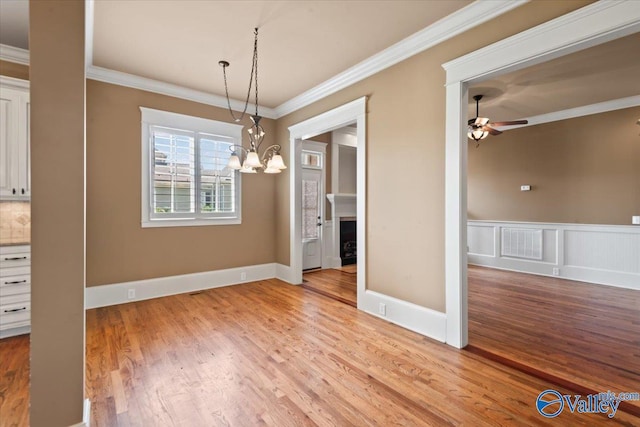 unfurnished dining area featuring crown molding, ceiling fan with notable chandelier, and light hardwood / wood-style flooring