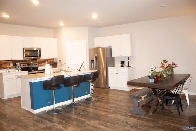 kitchen with a kitchen island with sink, tasteful backsplash, dark wood-type flooring, white cabinetry, and appliances with stainless steel finishes