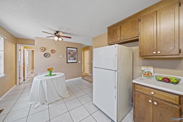 kitchen with brown cabinets, light countertops, freestanding refrigerator, light tile patterned flooring, and a textured ceiling