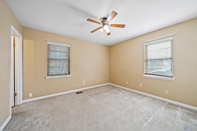 carpeted empty room featuring a textured ceiling, baseboards, visible vents, and a ceiling fan