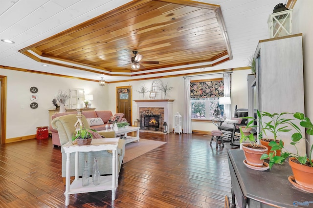 living room featuring wood ceiling, a stone fireplace, dark hardwood / wood-style flooring, a tray ceiling, and ceiling fan