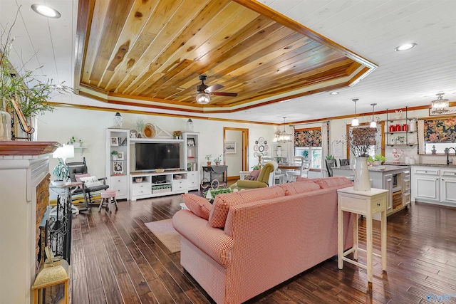 living room featuring crown molding, ceiling fan with notable chandelier, a tray ceiling, and dark wood-type flooring