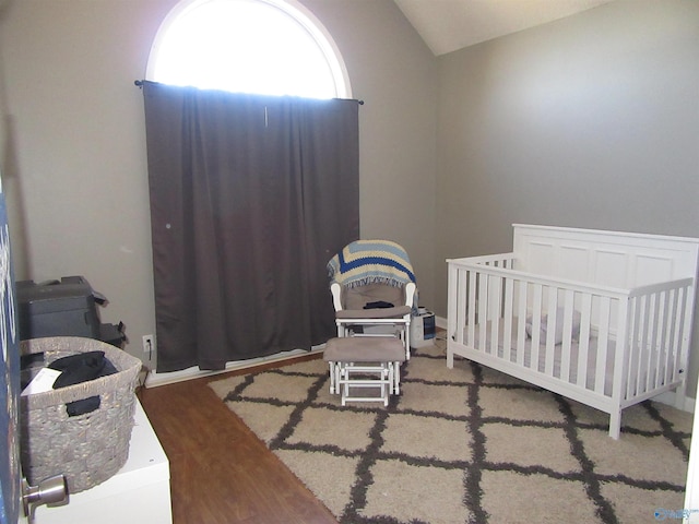 bedroom with a crib, vaulted ceiling, and wood finished floors