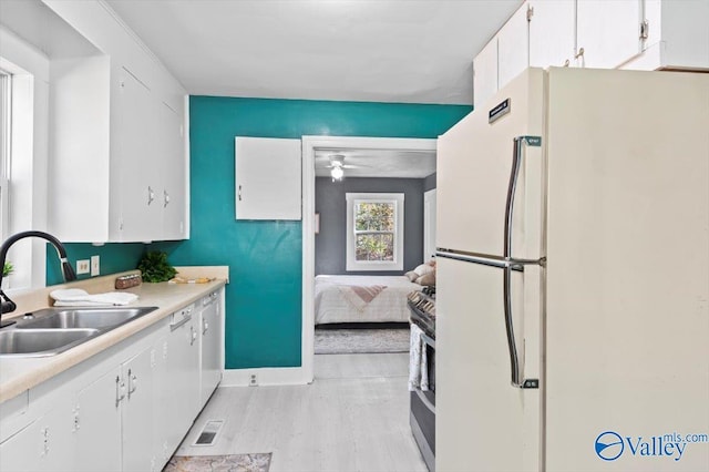 kitchen featuring freestanding refrigerator, light countertops, stainless steel range with gas cooktop, white cabinetry, and a sink