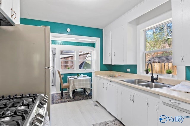 kitchen with stainless steel gas range oven, white cabinetry, light countertops, and a sink