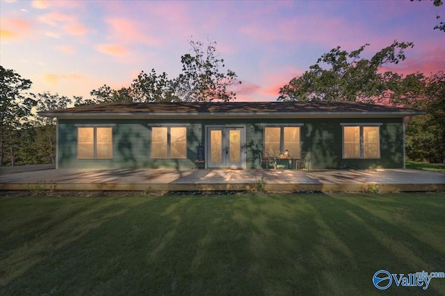 back house at dusk with a wooden deck and a lawn