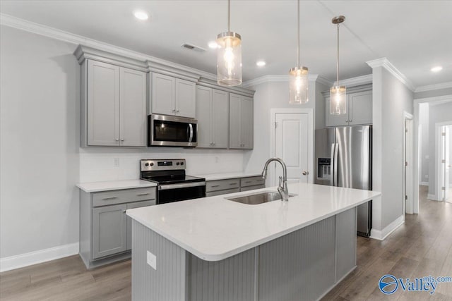 kitchen with sink, an island with sink, pendant lighting, wood-type flooring, and appliances with stainless steel finishes