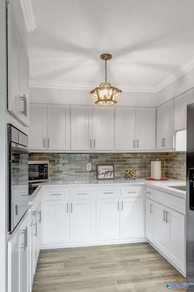 kitchen featuring appliances with stainless steel finishes, white cabinets, pendant lighting, and light hardwood / wood-style floors