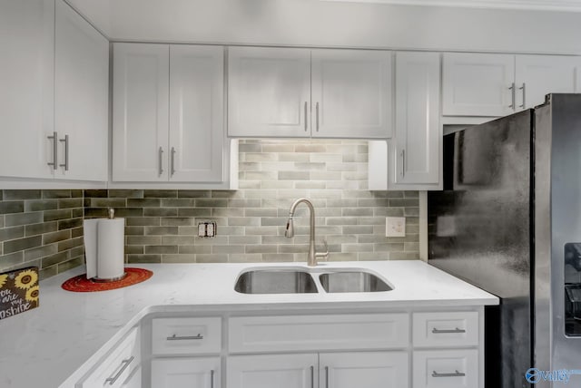 kitchen featuring sink, white cabinetry, decorative backsplash, and stainless steel refrigerator