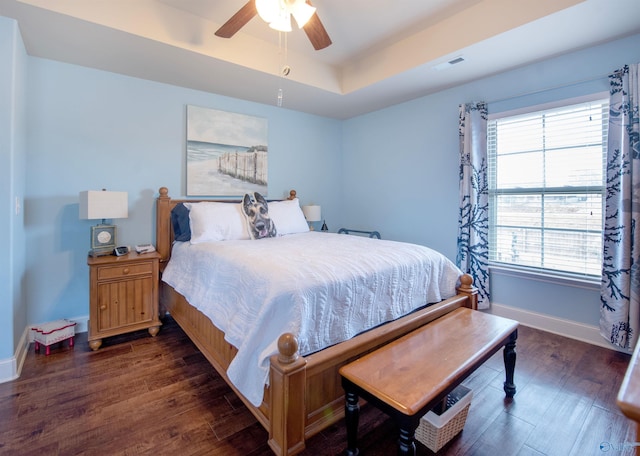 bedroom with baseboards, visible vents, a tray ceiling, and dark wood-type flooring