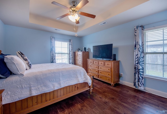 bedroom featuring visible vents, wood finished floors, baseboards, ceiling fan, and a tray ceiling