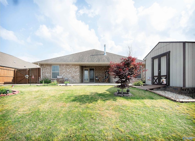 back of house featuring a lawn, fence, an outbuilding, and brick siding