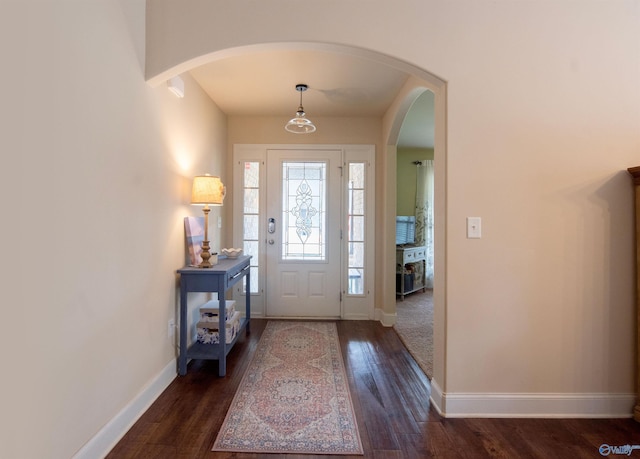 entryway with dark wood-style flooring, arched walkways, and baseboards