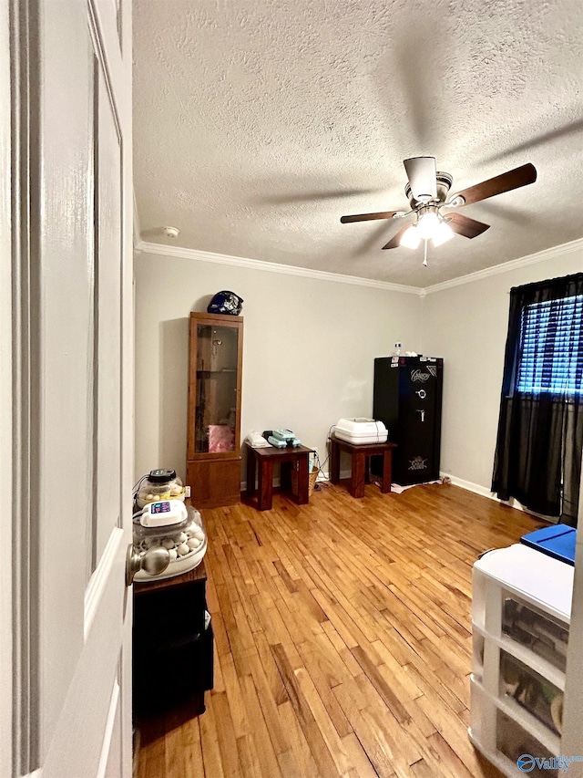 interior space featuring ceiling fan, a textured ceiling, ornamental molding, and wood finished floors