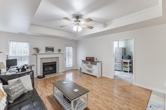 living room featuring ornamental molding, a raised ceiling, ceiling fan, and light wood-type flooring