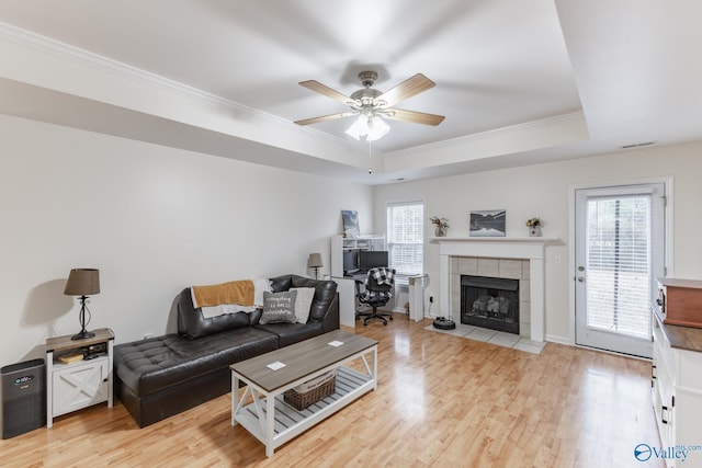 living room featuring crown molding, a tray ceiling, light hardwood / wood-style floors, and a tile fireplace