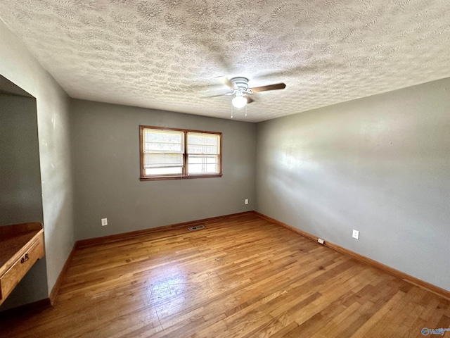 unfurnished room with visible vents, a textured ceiling, wood finished floors, baseboards, and ceiling fan