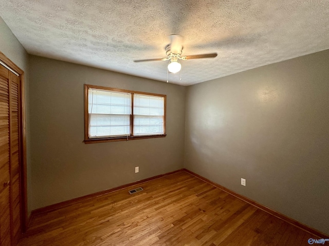 spare room with visible vents, a textured ceiling, wood finished floors, baseboards, and ceiling fan