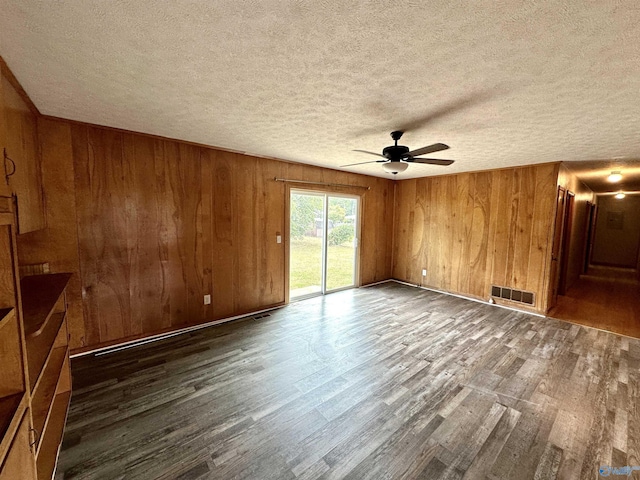 spare room featuring visible vents, wood walls, wood finished floors, a textured ceiling, and a ceiling fan