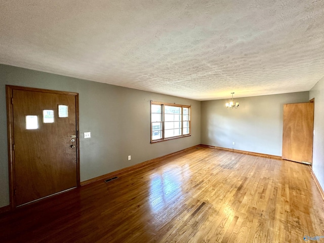 foyer entrance with wood finished floors, baseboards, visible vents, a textured ceiling, and a chandelier