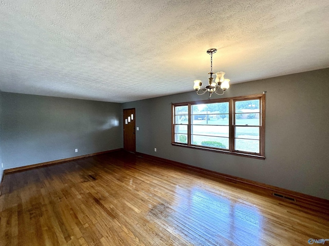 spare room with visible vents, baseboards, a chandelier, wood finished floors, and a textured ceiling