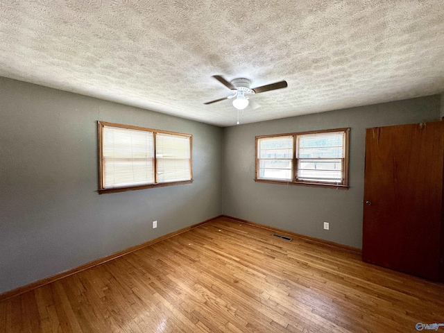 unfurnished bedroom featuring visible vents, baseboards, light wood-style flooring, a textured ceiling, and a ceiling fan