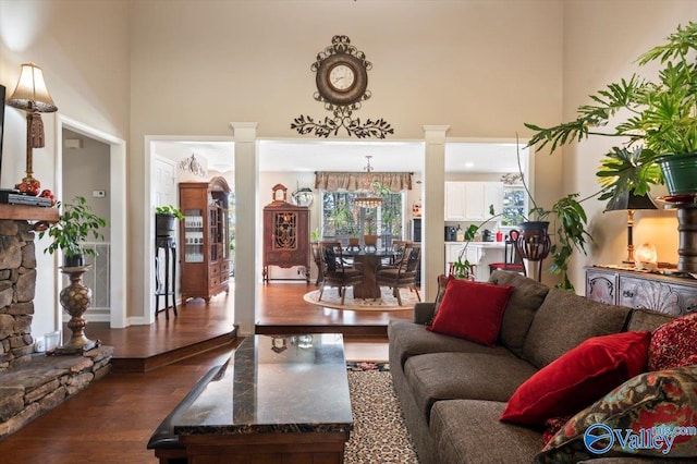 living room featuring decorative columns, a towering ceiling, and dark wood-type flooring