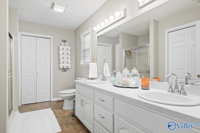 bathroom featuring vanity, toilet, a shower with door, and a textured ceiling