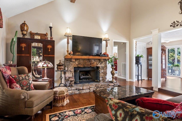 living room with hardwood / wood-style flooring, a stone fireplace, lofted ceiling, and decorative columns