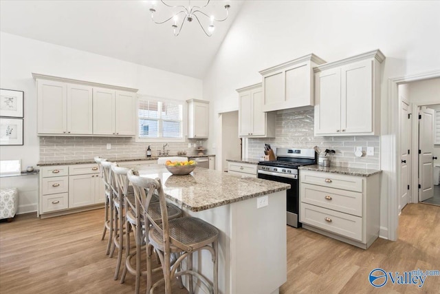 kitchen with high vaulted ceiling, light hardwood / wood-style flooring, light stone countertops, appliances with stainless steel finishes, and a kitchen island