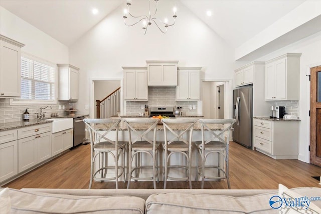 kitchen with backsplash, high vaulted ceiling, sink, light wood-type flooring, and stainless steel appliances