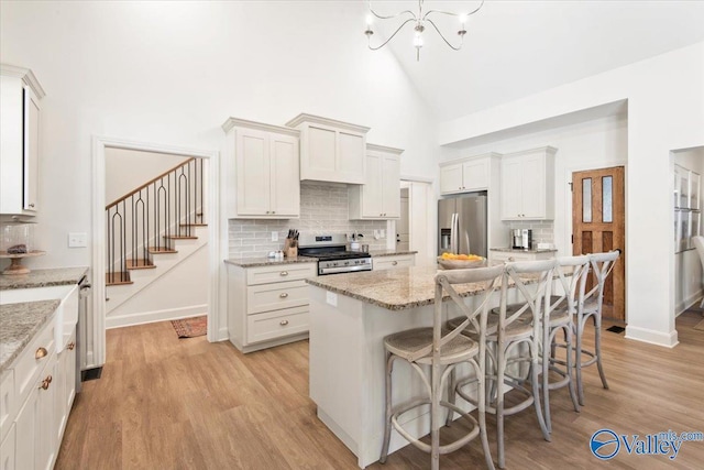 kitchen with light stone counters, high vaulted ceiling, light hardwood / wood-style floors, white cabinets, and appliances with stainless steel finishes