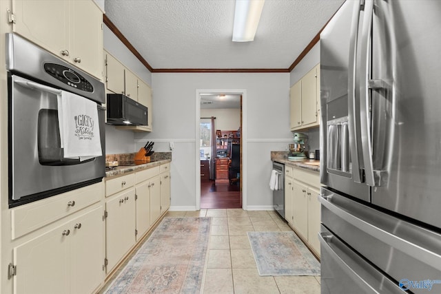 kitchen with light tile patterned floors, cream cabinets, appliances with stainless steel finishes, ornamental molding, and a textured ceiling