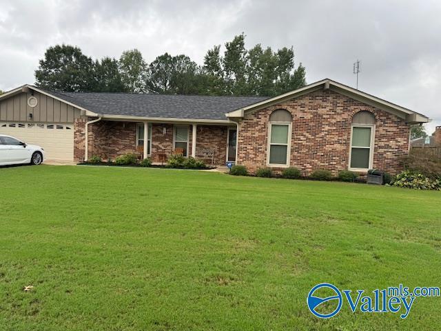 ranch-style home featuring board and batten siding, a front yard, brick siding, and an attached garage