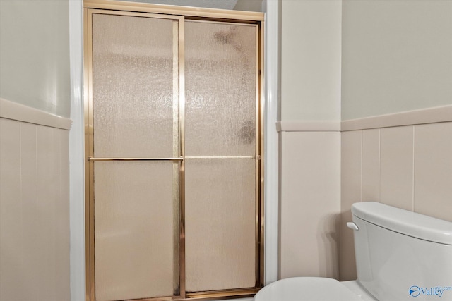 full bath with wainscoting, a shower with door, and toilet