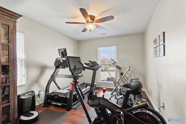 workout room with a textured ceiling, wood finished floors, visible vents, a ceiling fan, and baseboards